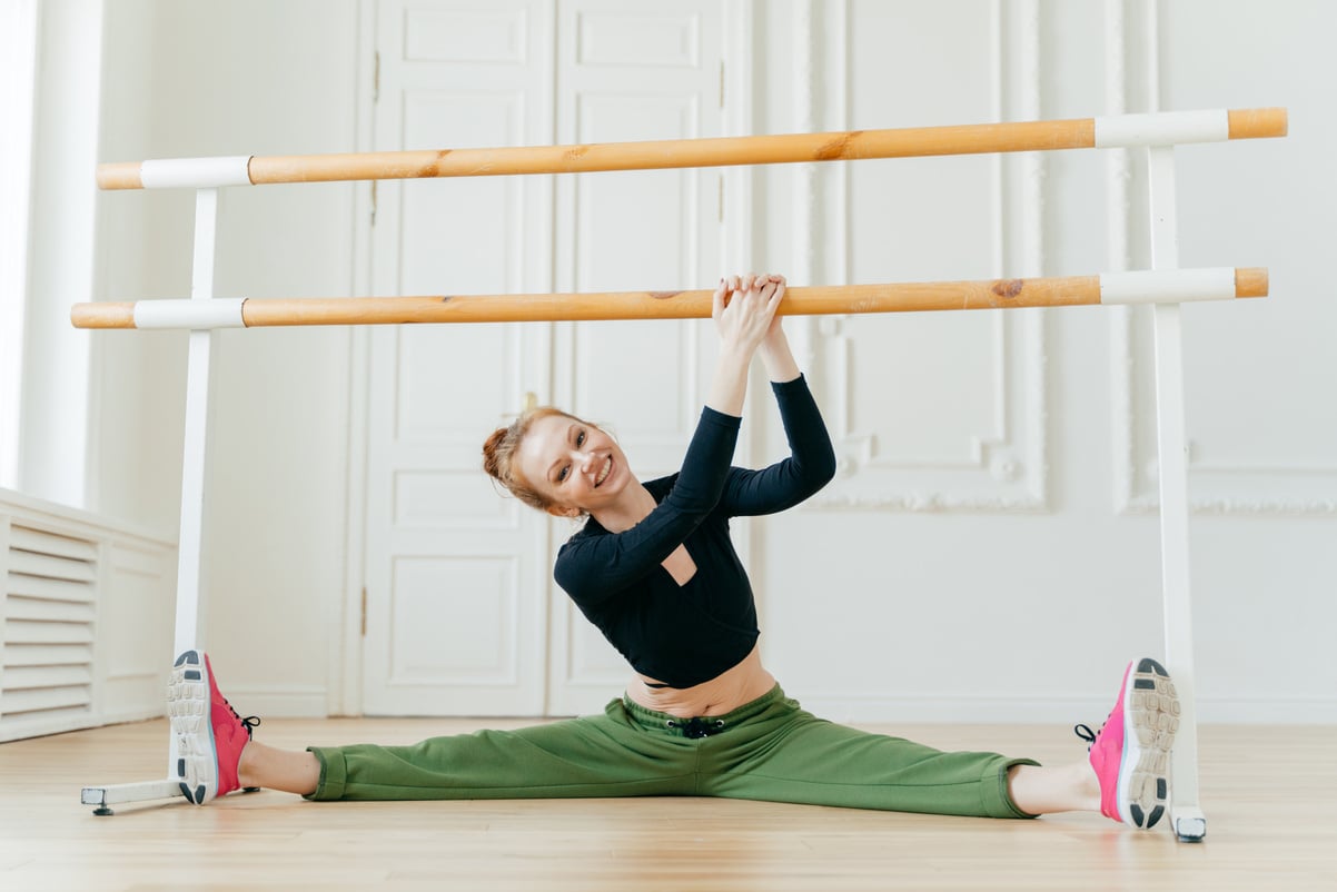 Caucasian female ballerina spreads legs sideways, shows spli